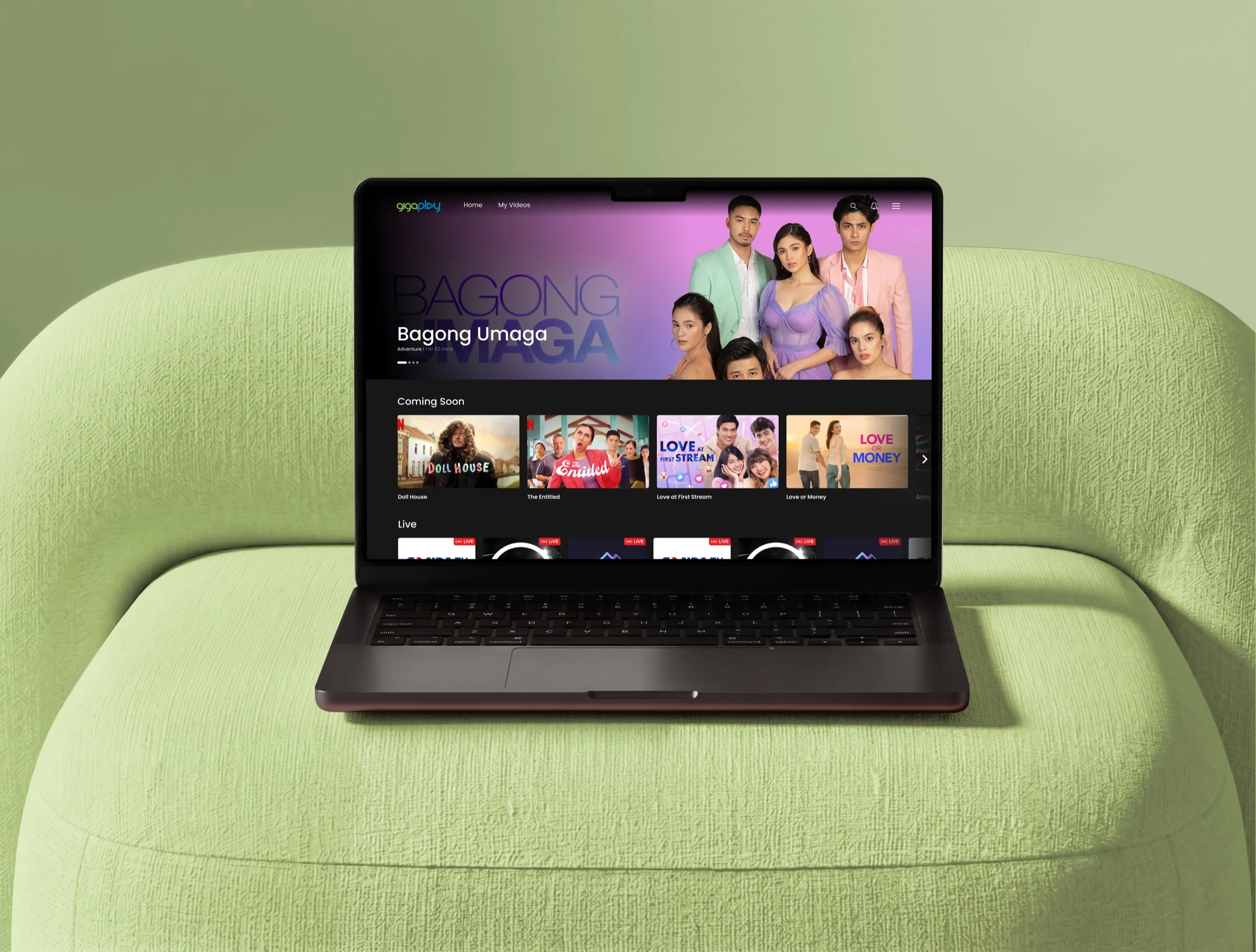 Gigaplay's streaming home on a laptop resting on a green boucle chair: Bagong Umaga in the hero and Coming Soon below.